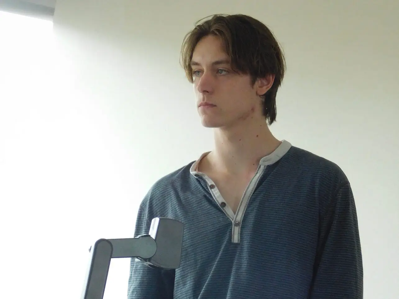 Standing beside a desk, a young man looks to the side next to a tablet.