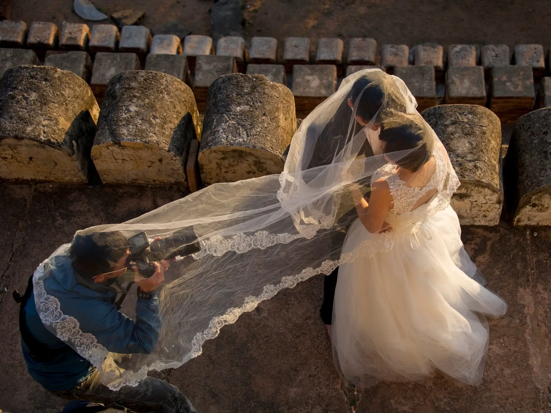 A photographer takes a photo of a bride and groom from underneath the bride's veil.