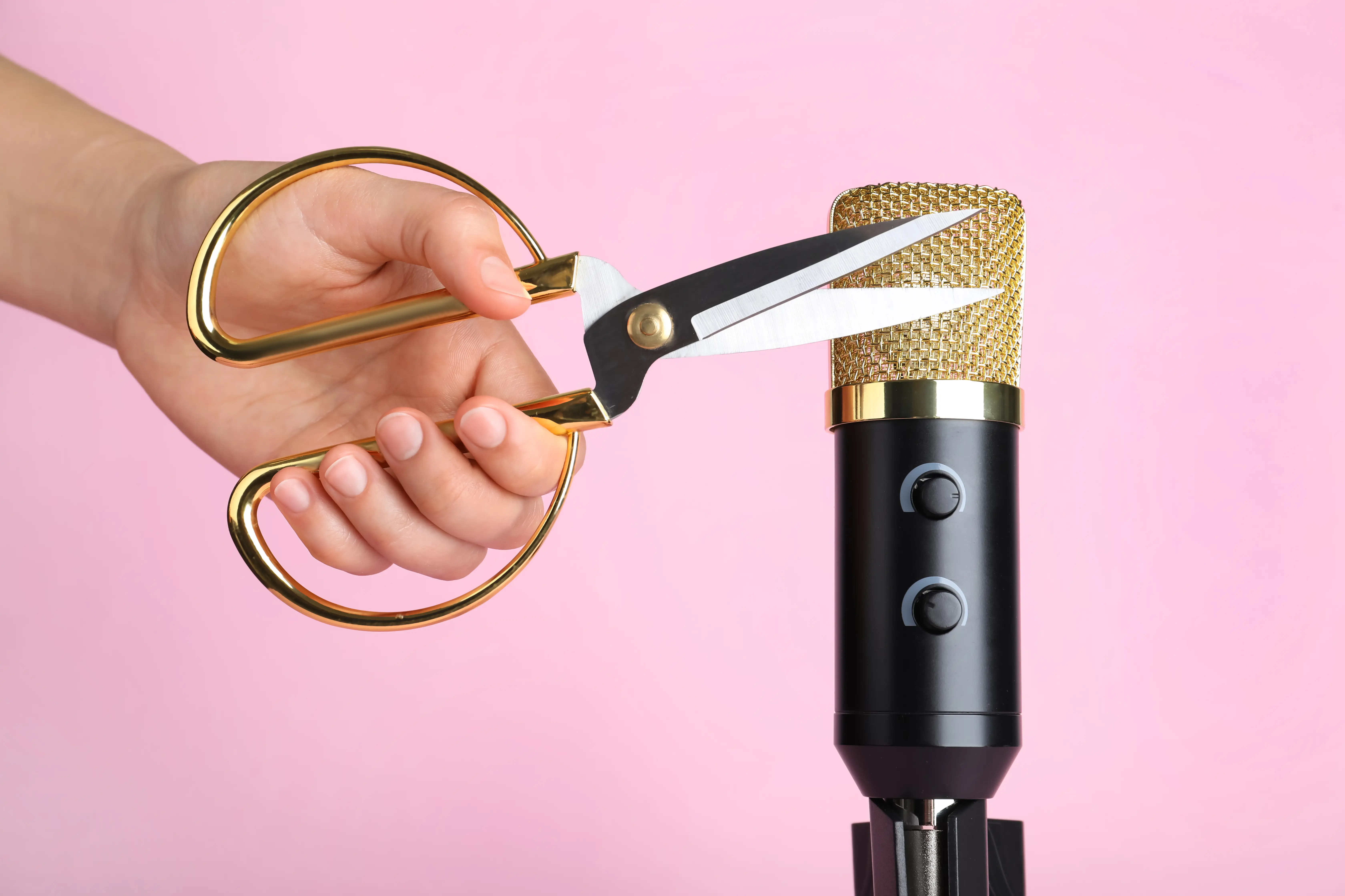 A pair of scissors near a microphone in front of a pink background.