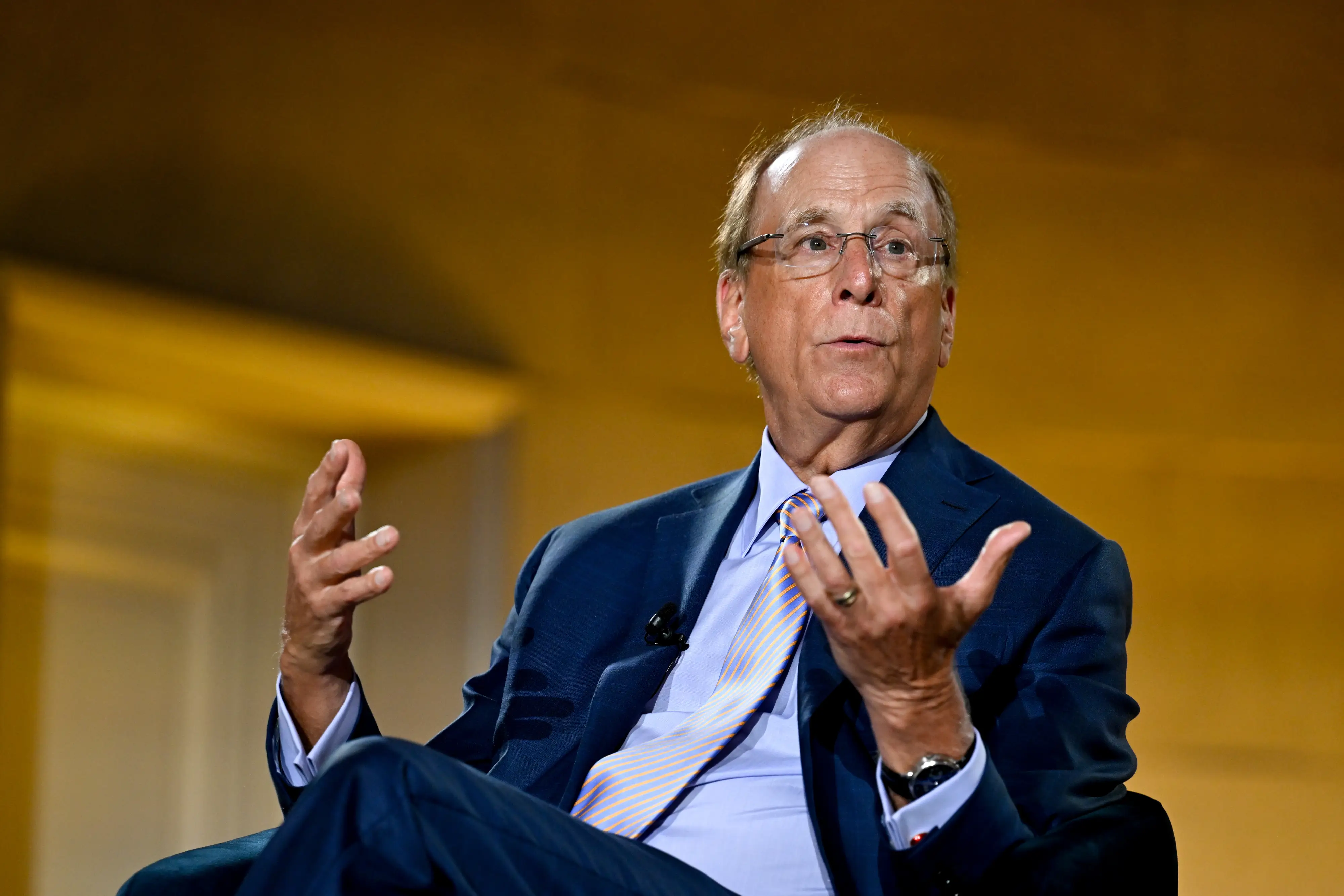 Blackrock CEO Larry Fink wearing is sitting on a chair while speaking.