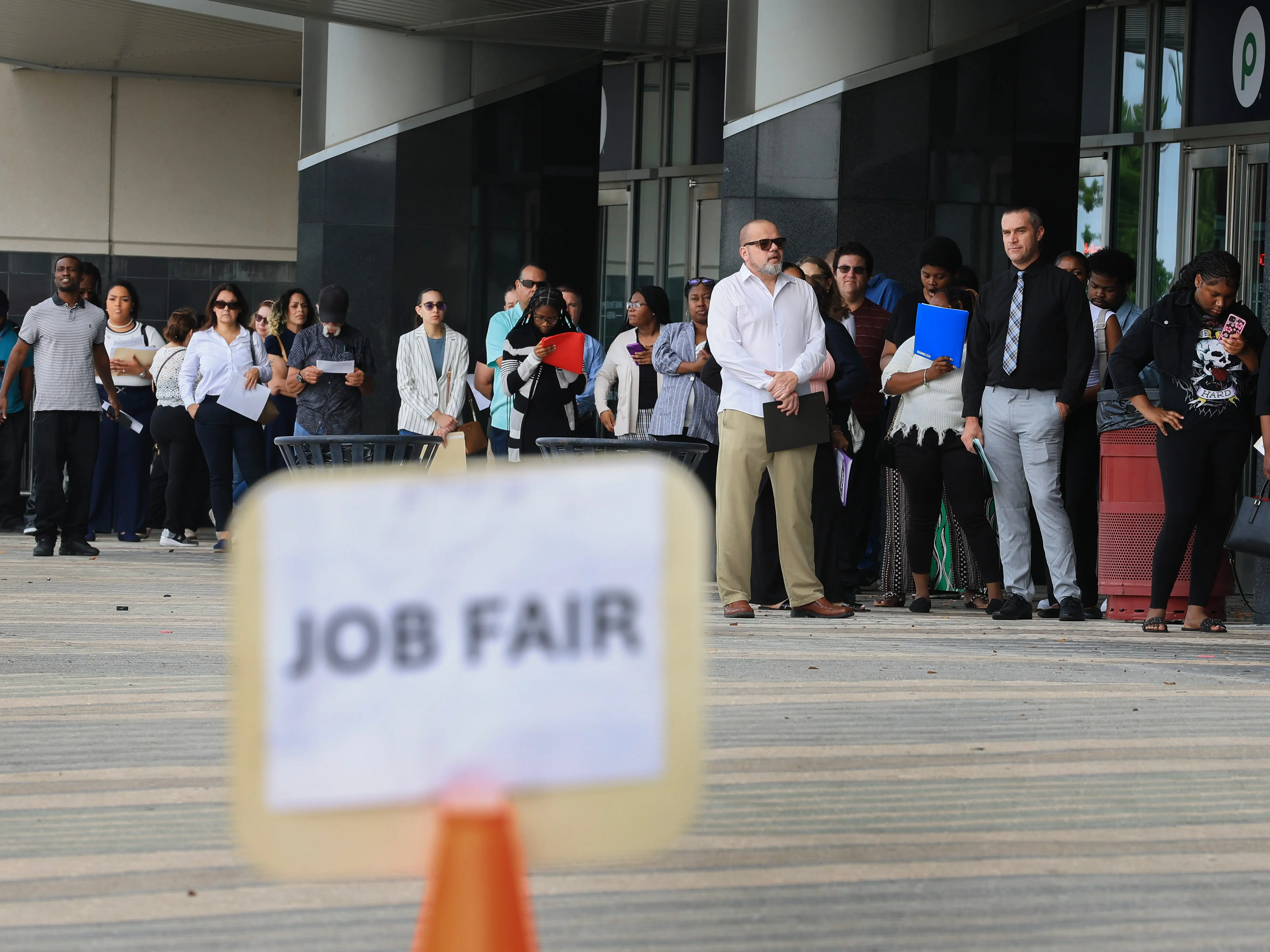 A line of people, carrying folders and in semi-formal wear, outside of a job fair.