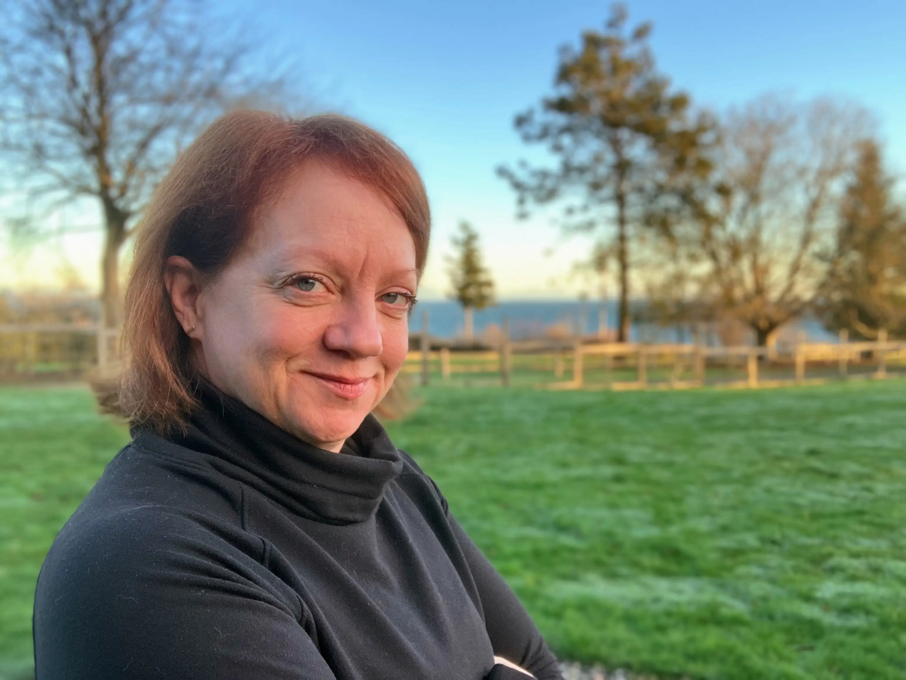 Woman smiling in front of trees, grass