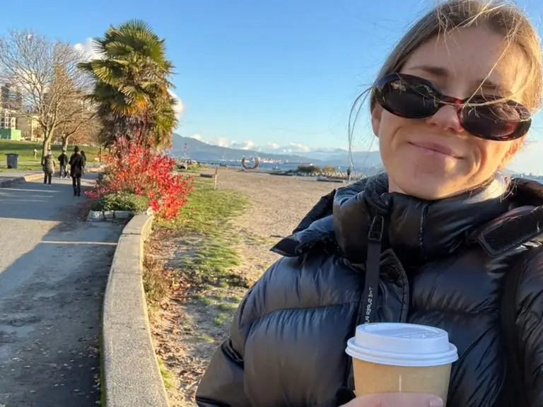 Woman in sunglasses holding coffee, smiling on trail