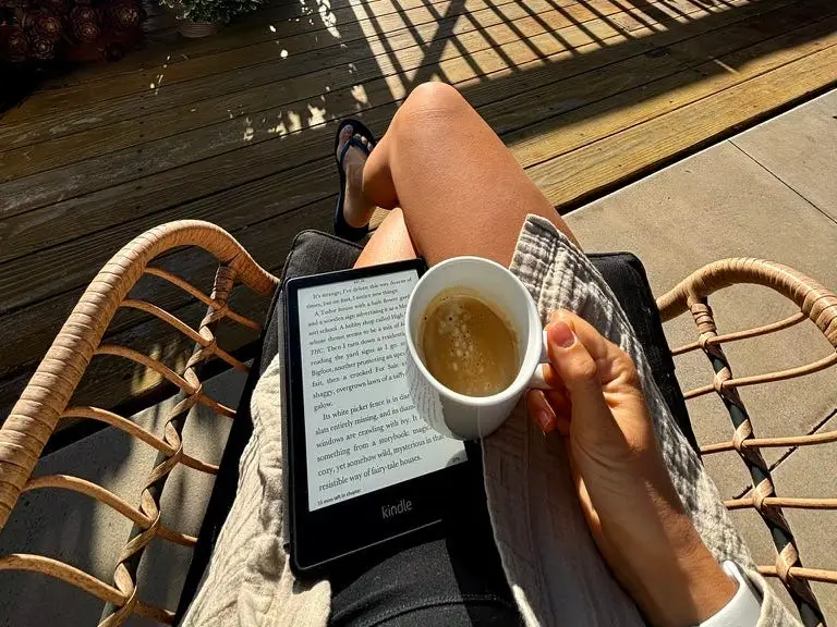 Perosn holding e-reader, coffee, on sunny balcony