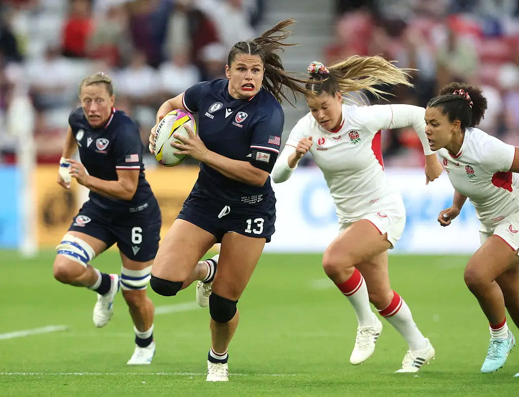 Ilona Maher on the field with the ball, running with a teammate against two opponents in a rugby match against England in the World Cup