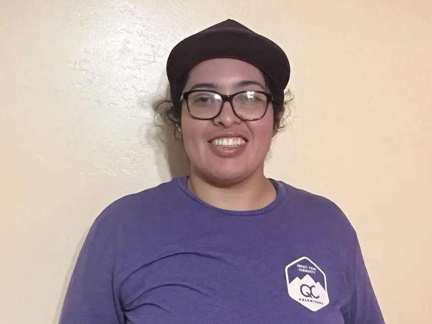 Sandra Navarro, who assembles furniture for Taskrabbit, wears a purple t-shirt and dark baseball cap while posing against a beige background.