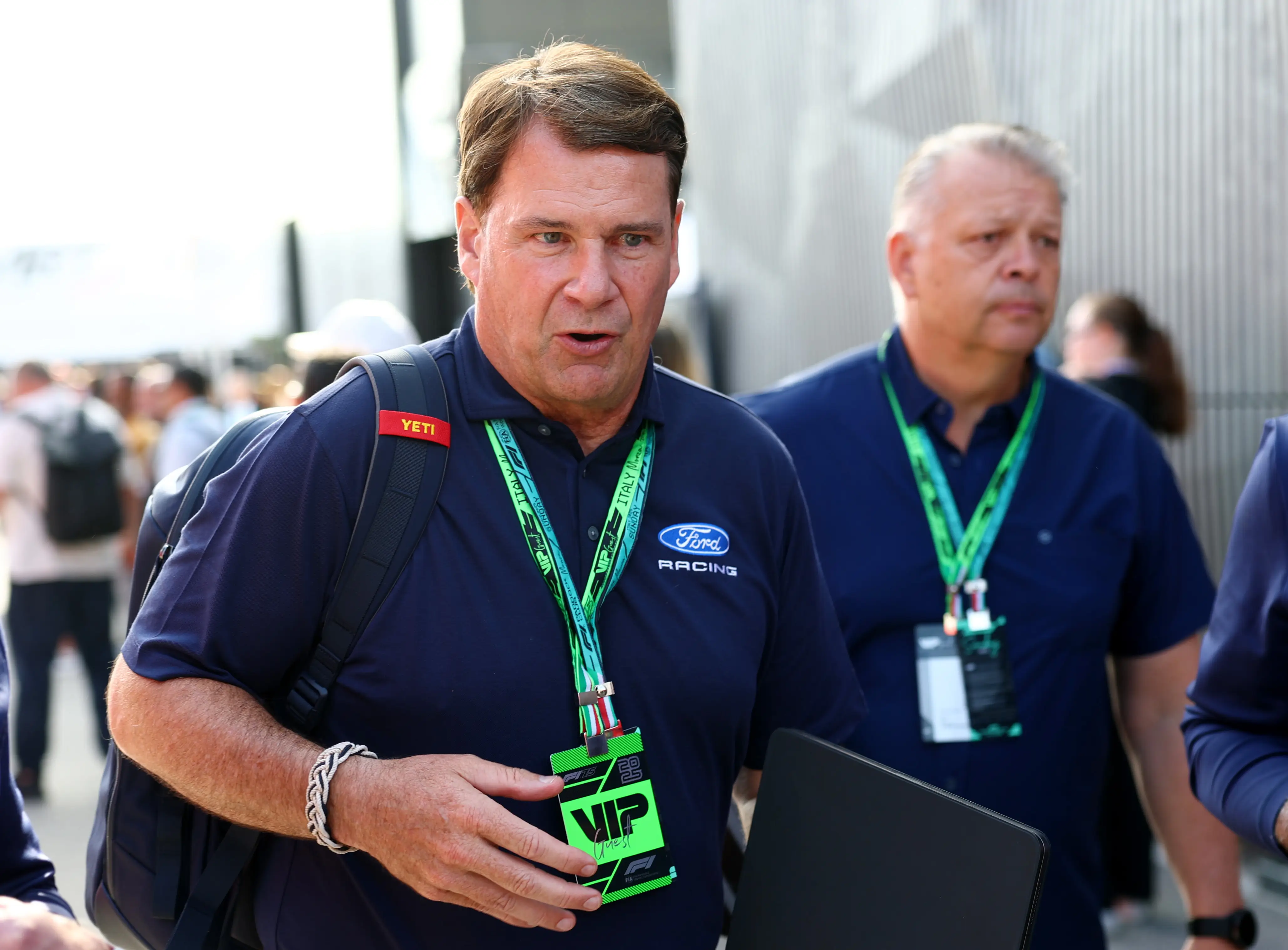 Jim Farley, wearing a blue Ford Racing polo and a VIP tag, walks outside during a crowded event.