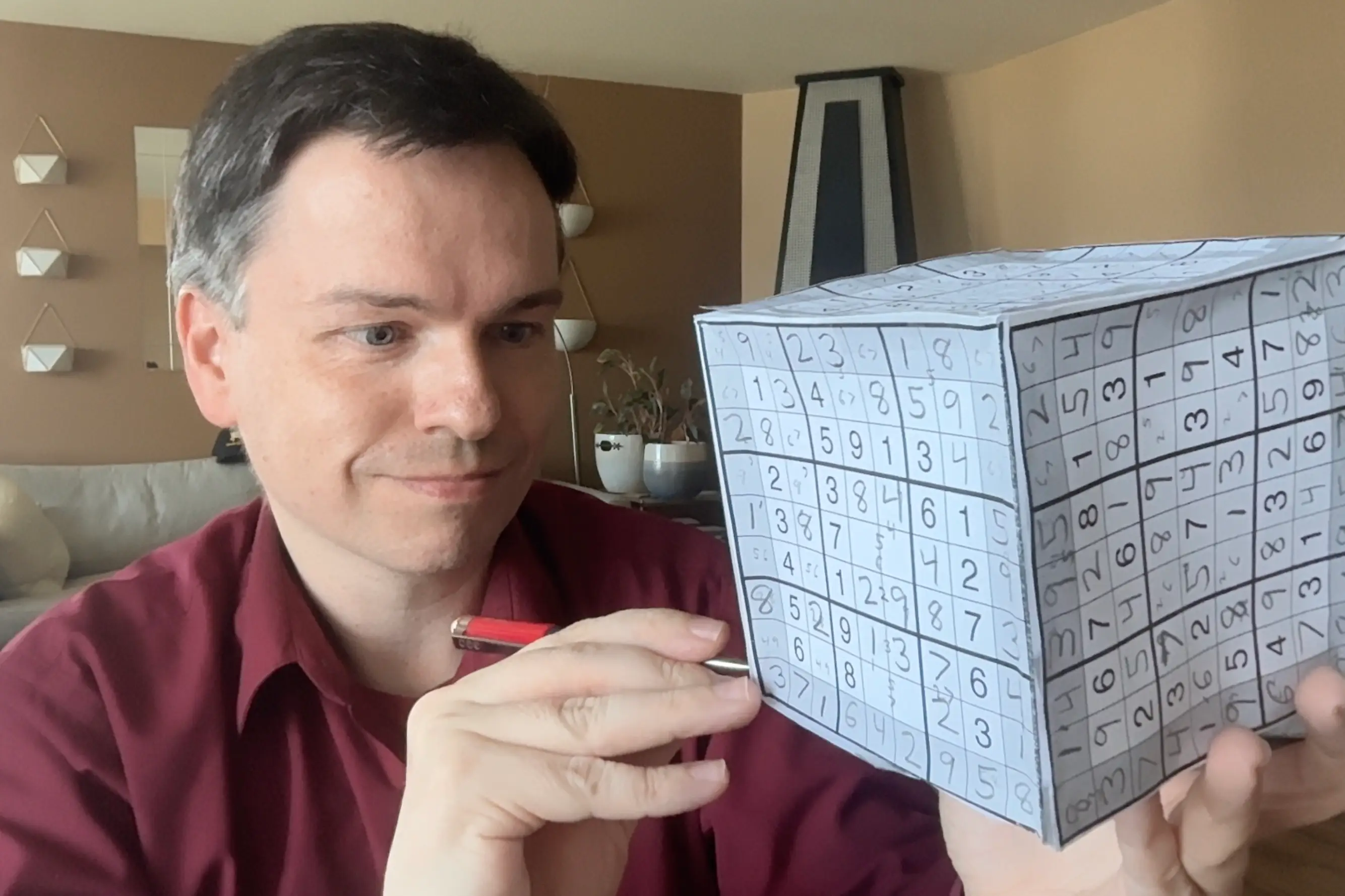 A man holds a pen and a 3D Sudoku box.