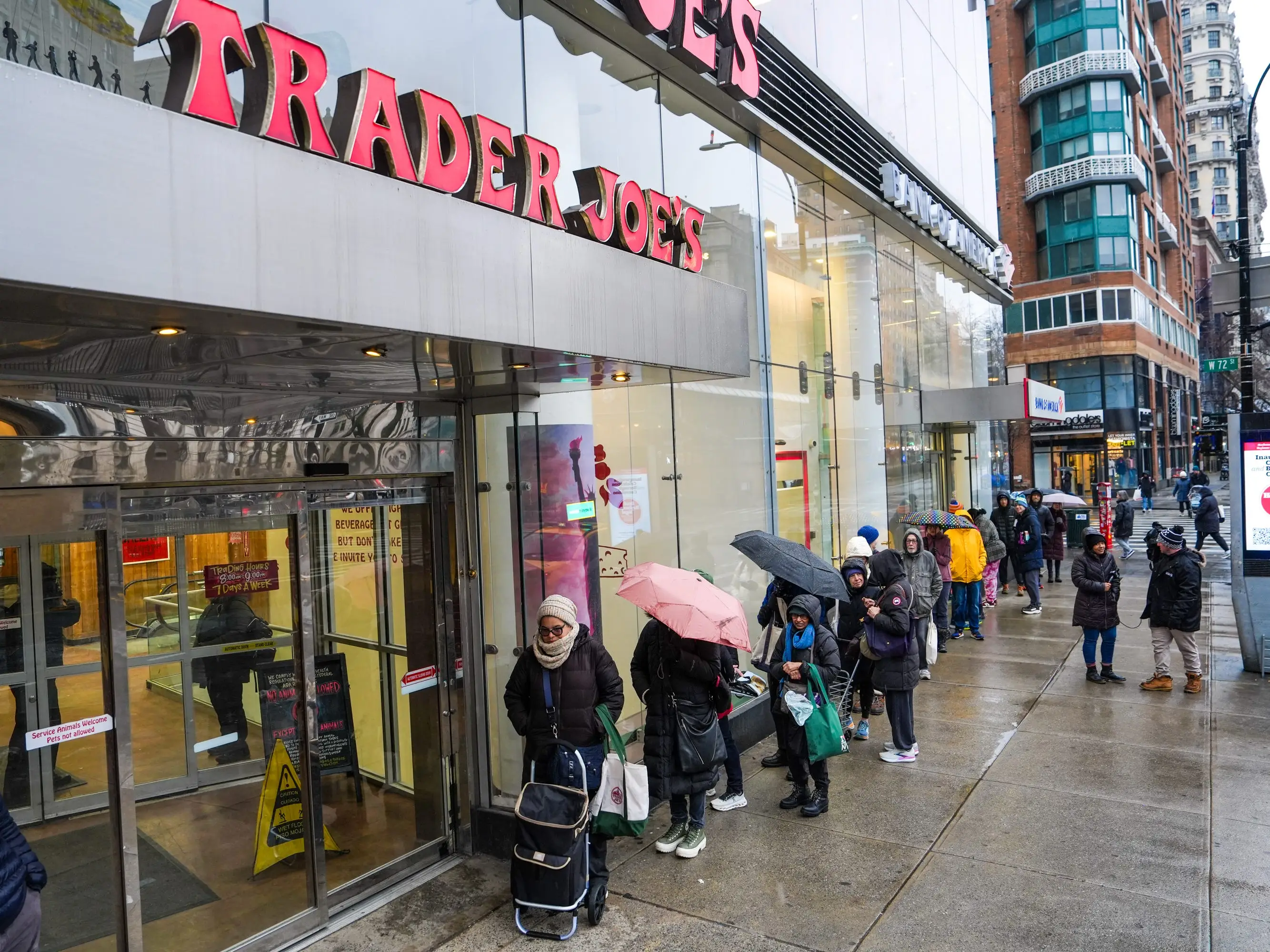 People wait in line with umbrellas in the rain for a Trader Joe's grocery store to open in New York City.