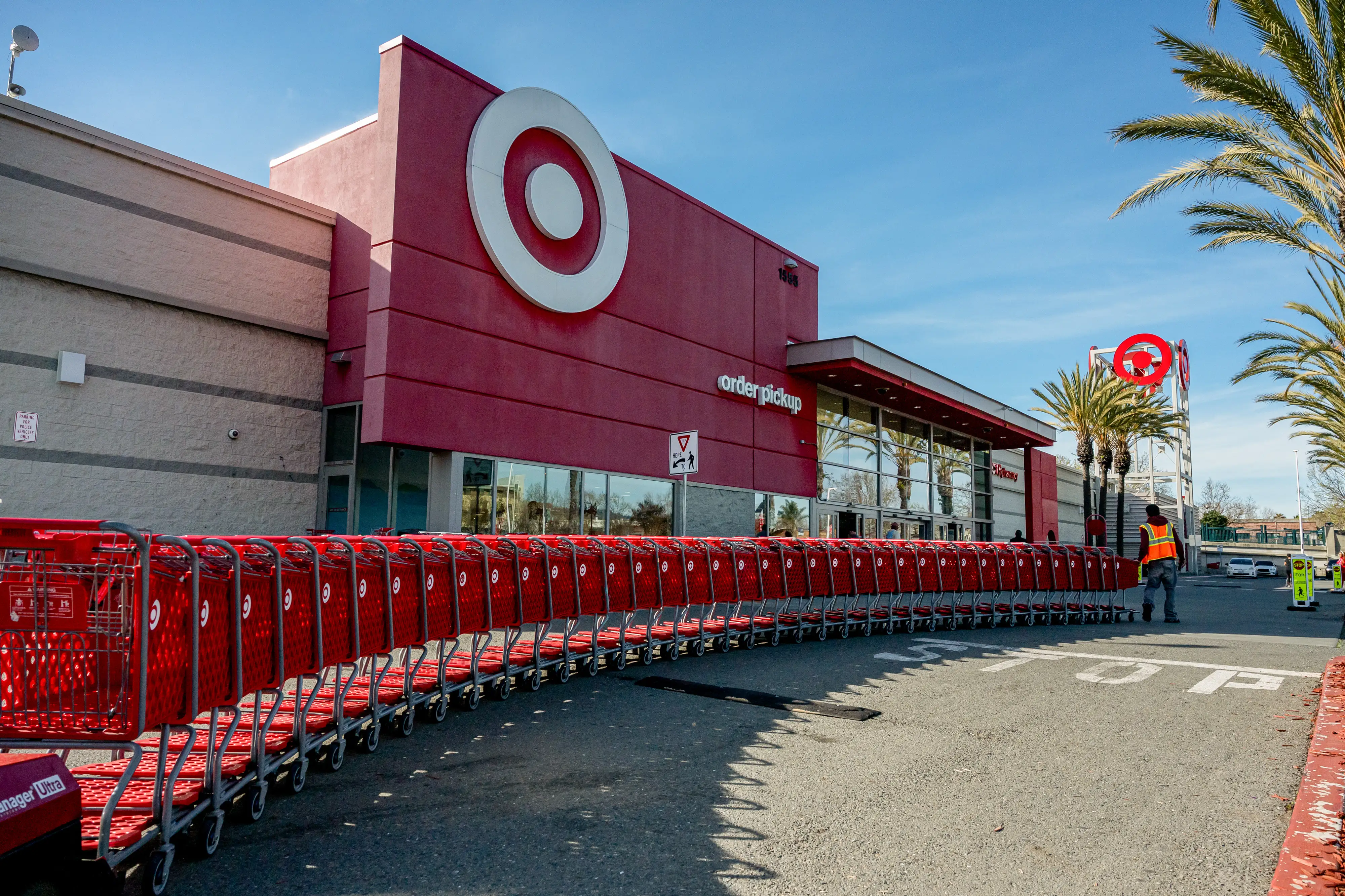 A cart attendant pulls a line of red carts toward the front doors of a Target store.