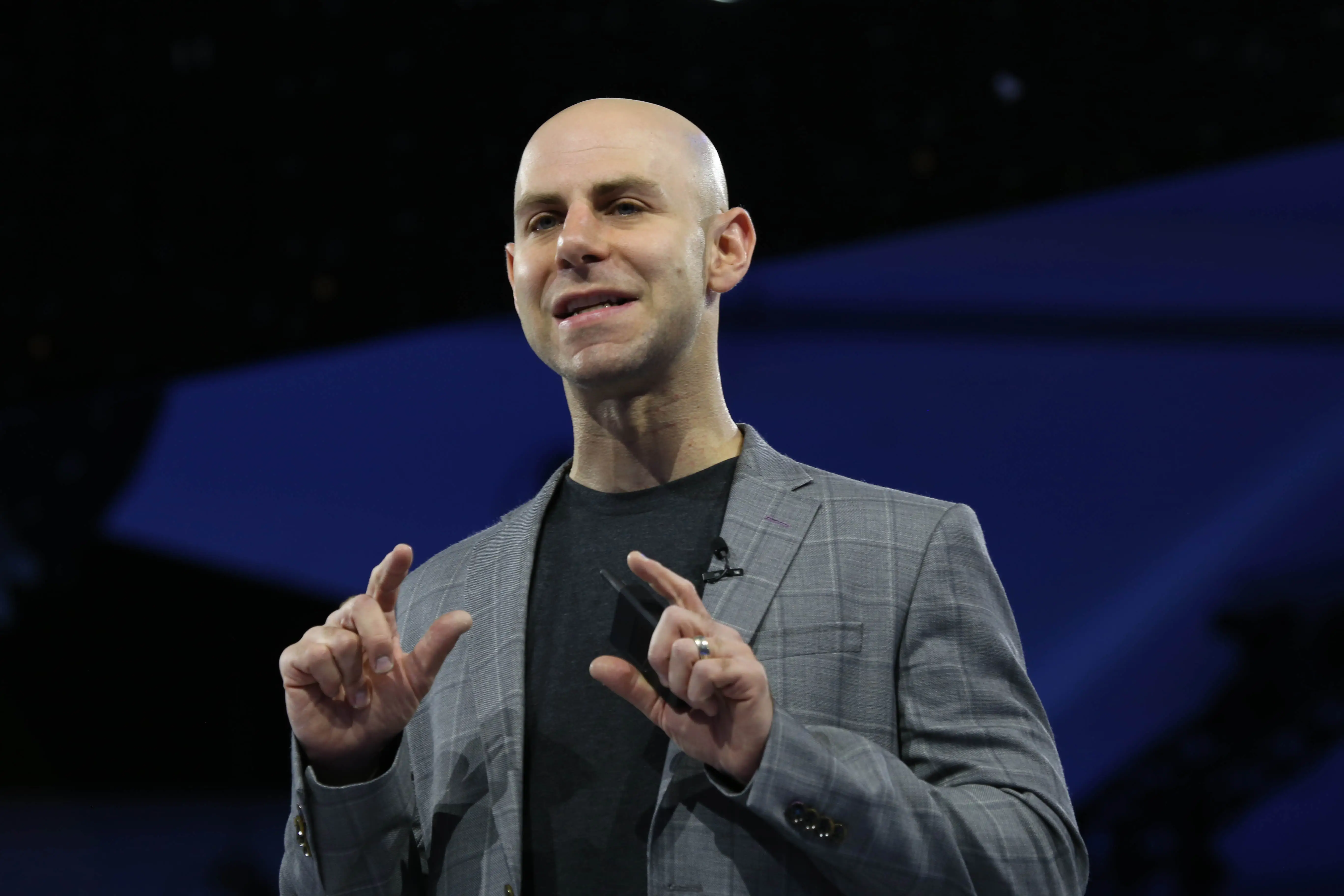 Adam Grant speaks on stage in a grey blazer and a black shirt
