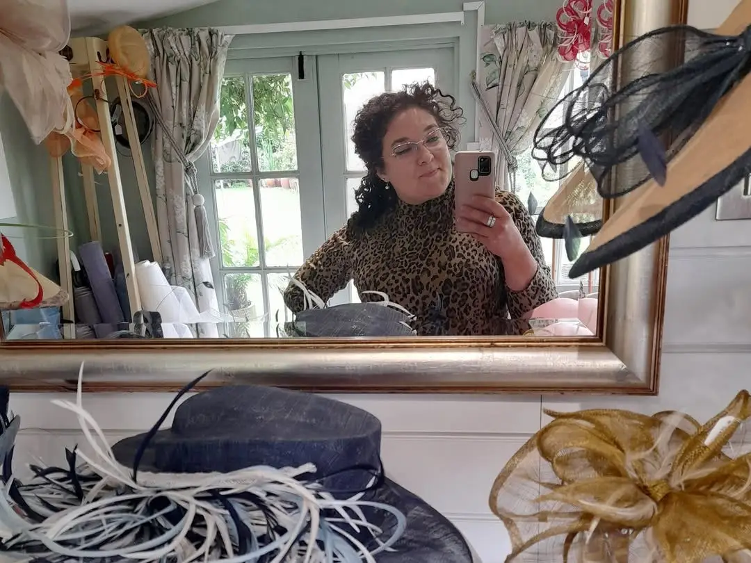 A woman. taking s cellphone picture in a millinery studio