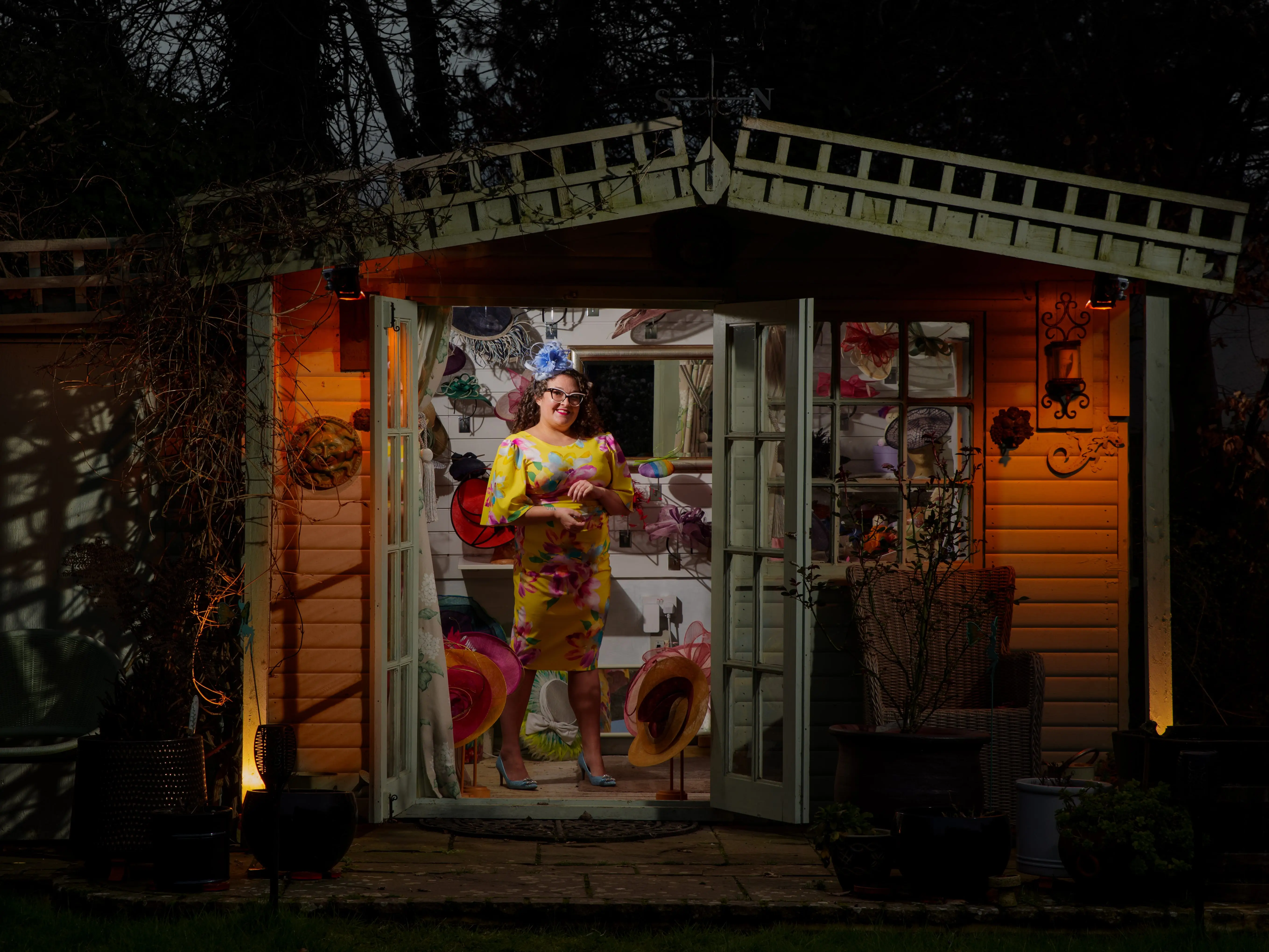 A woman in a yellow dress inside a garden shed full of hats