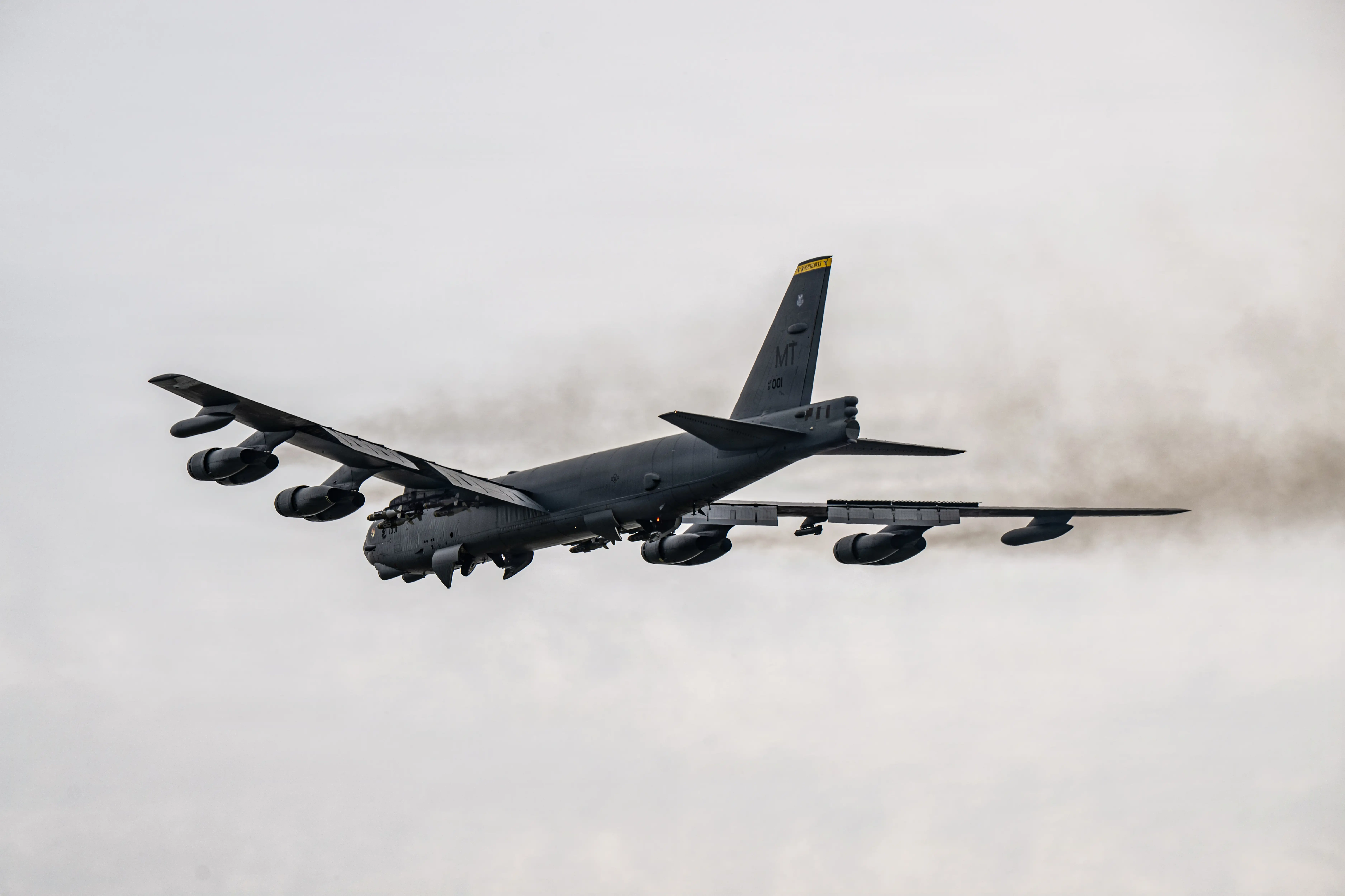 A US Air Force B-52 Stratofortress flies in an overcast grey sky.