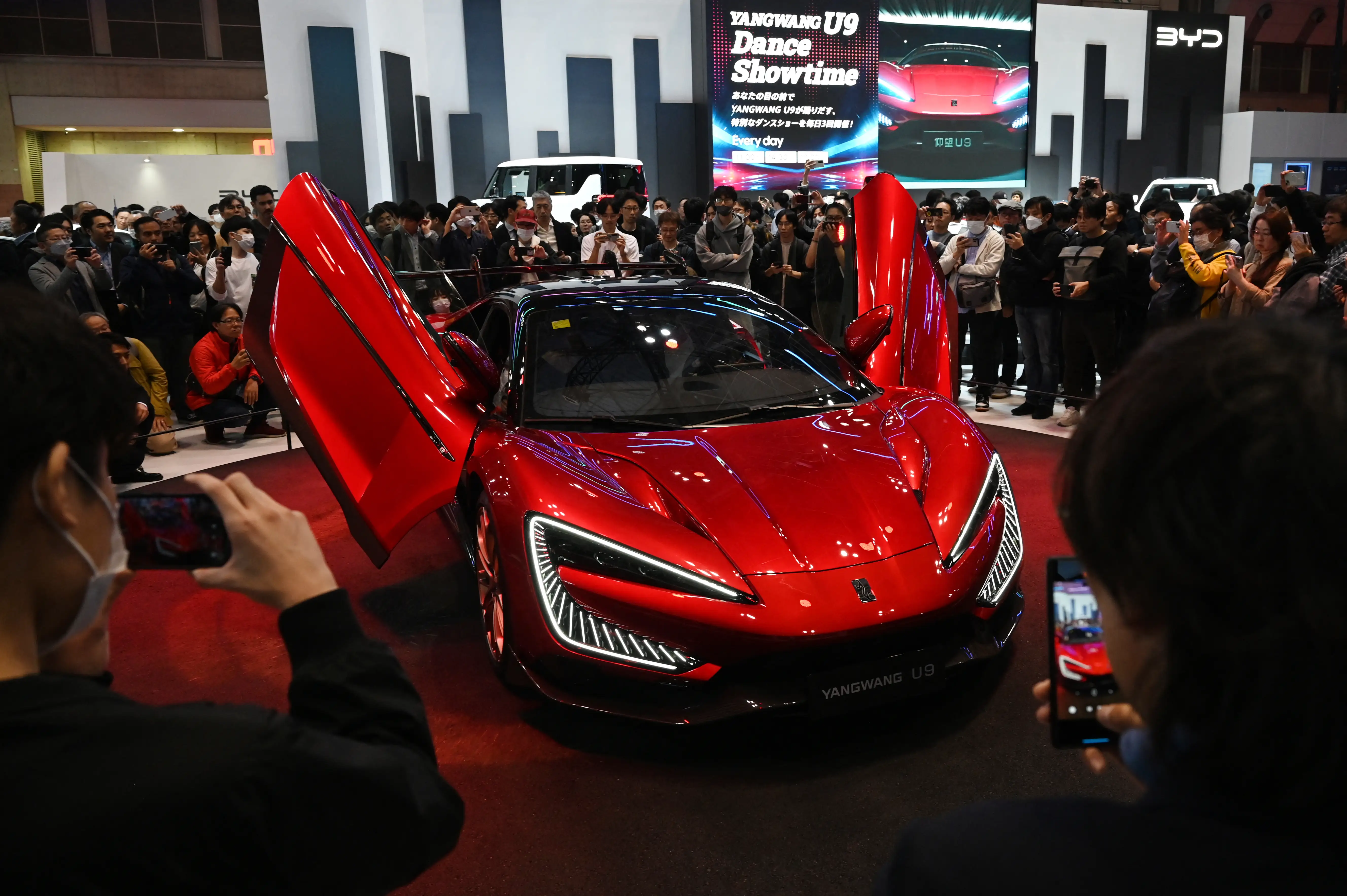 A red Yangwang U9 sports car at an auto show with its doors open.