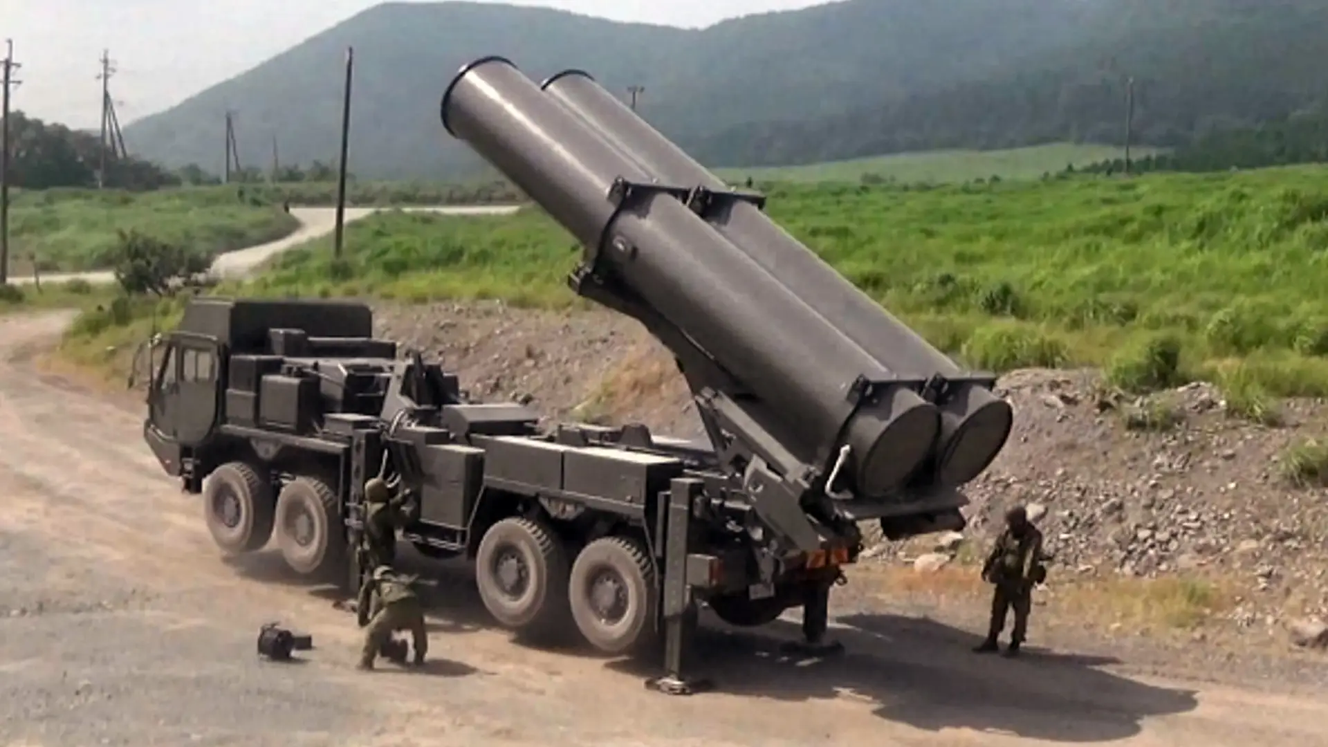 Men stand around a truck with missile launchers on the back located in a field.