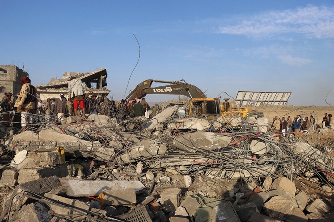 photo of people and heavy machinery on large field of concrete rubble and rebar