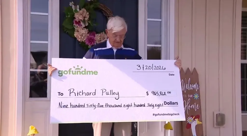 A 78-year-old DoorDash driver, Richard Pulley, holds up a large novelty check for $965,868.00 from GoFundMe.