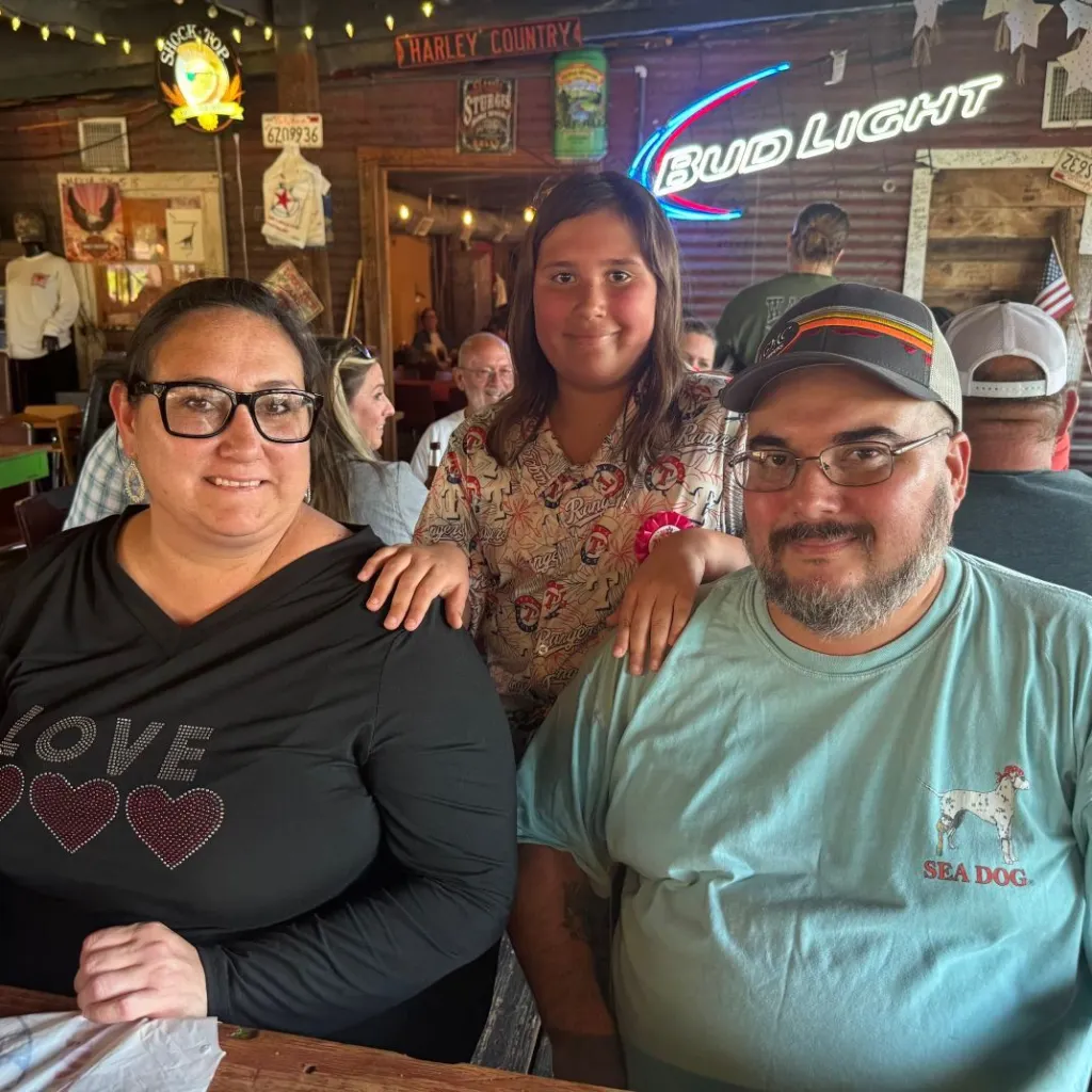 A young girl smiling with her arm around her parents' shoulders.