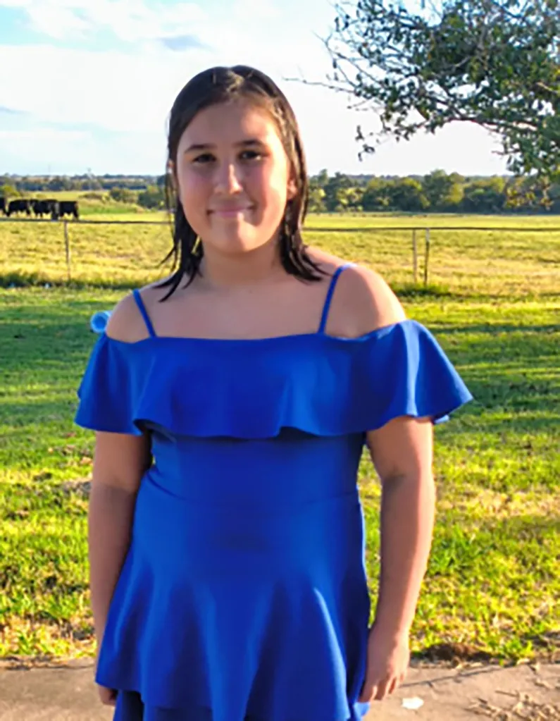JackLynn Blackwell, a 9-year-old girl, standing outdoors in a bright blue dress.