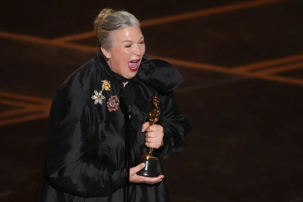 Kate Hawley holding an Oscar statuette and speaking into a microphone.