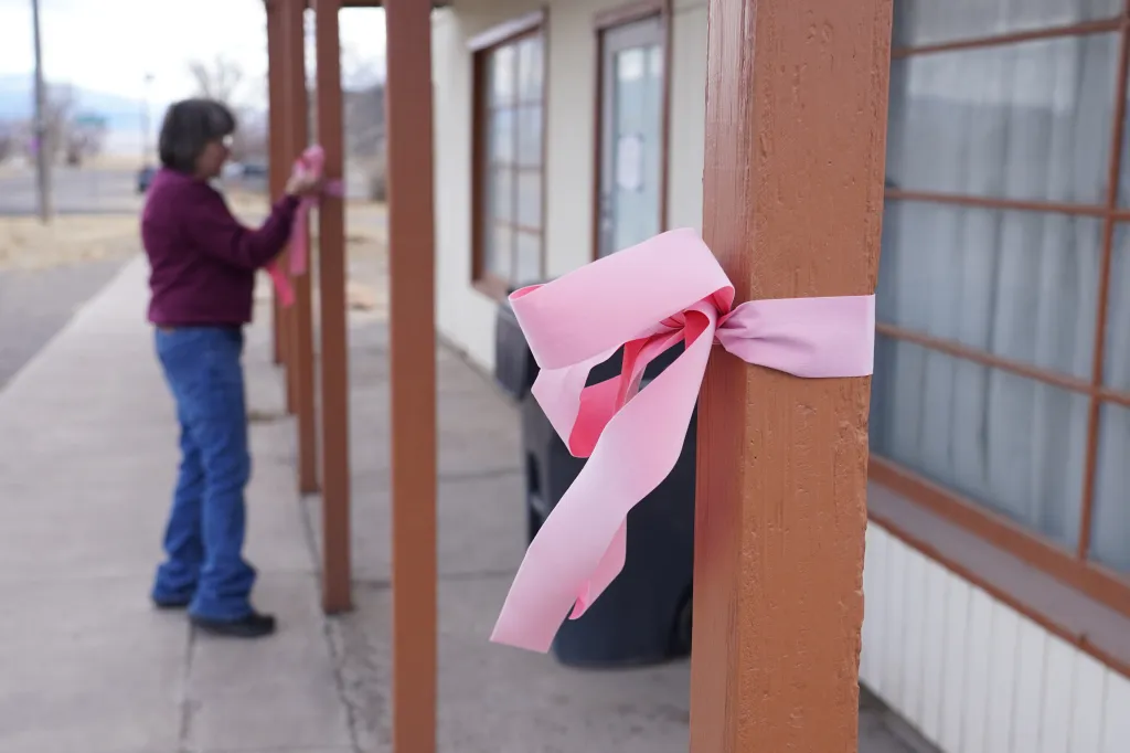 A woman hangs a pink ribbon on a pole Thursday, March 5, 2026, in Lyman, Utah, in honor of a woman that was killed a day earlier.
