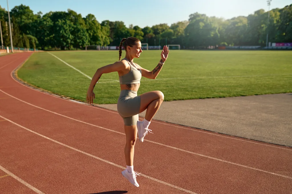 Athletic woman doing high knees workout on track at sunrise.