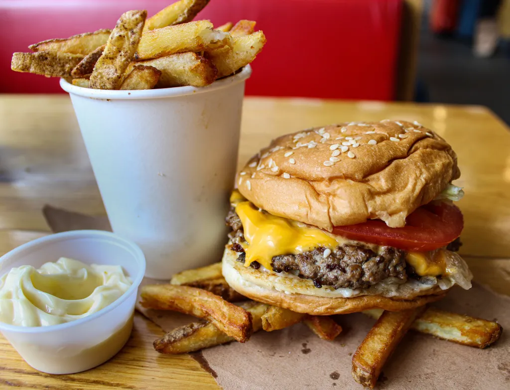 A Five Guys cheeseburger, cup of fries, and a small cup of mayonnaise on a wooden table.
