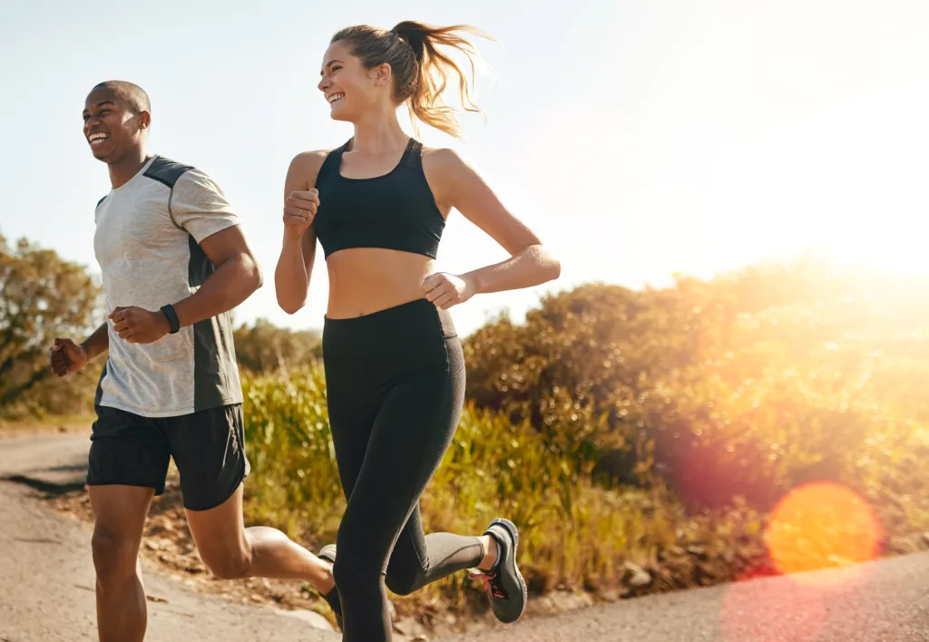 Two happy runners, a man and a woman, running outdoors during the day.