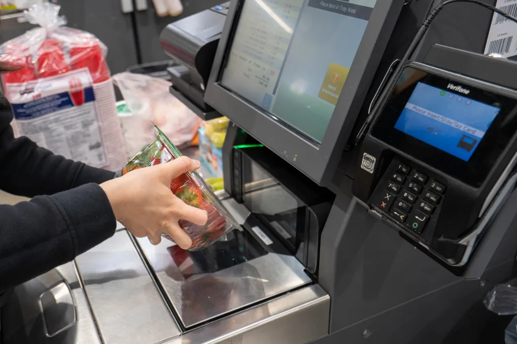 A shopper scanning a box of strawberries at a self-checkout lane in a Costco store.