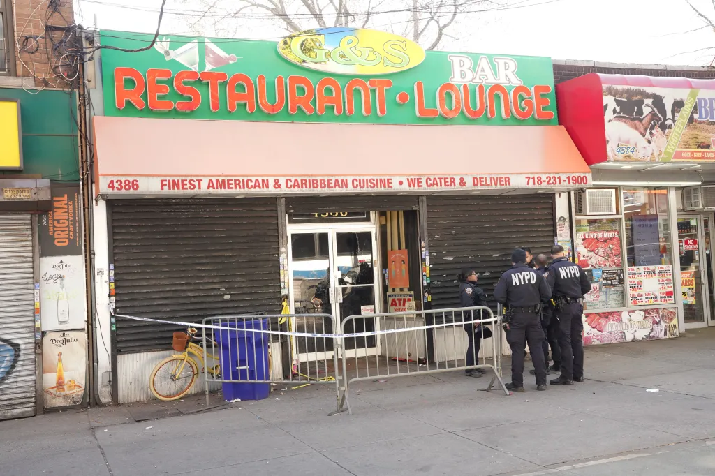Police officers stand outside a restaurant and bar, with yellow caution tape indicating a crime scene.