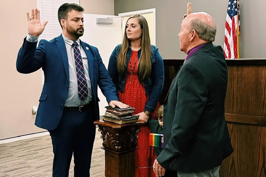 Ernie Yarbrough being sworn in with his hand on a stack of books, alongside a woman, and a man administering the oath.