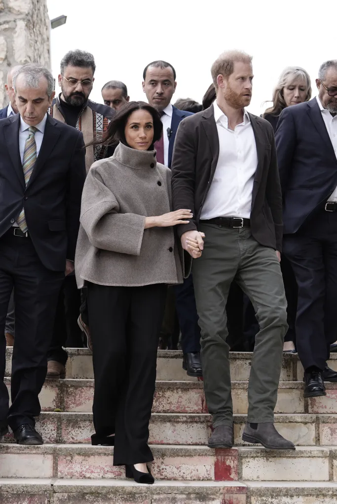 Meghan Markle and Prince Harry descend stairs, holding hands, surrounded by others.