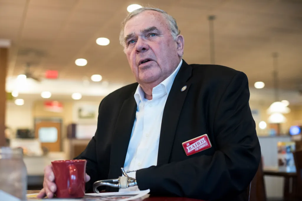 Jim Baird, candidate for Congress, sits at a table with a red mug and prosthetic arm.