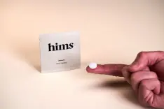 A pill pack with the word Hims on the front and a finger holding a pill.