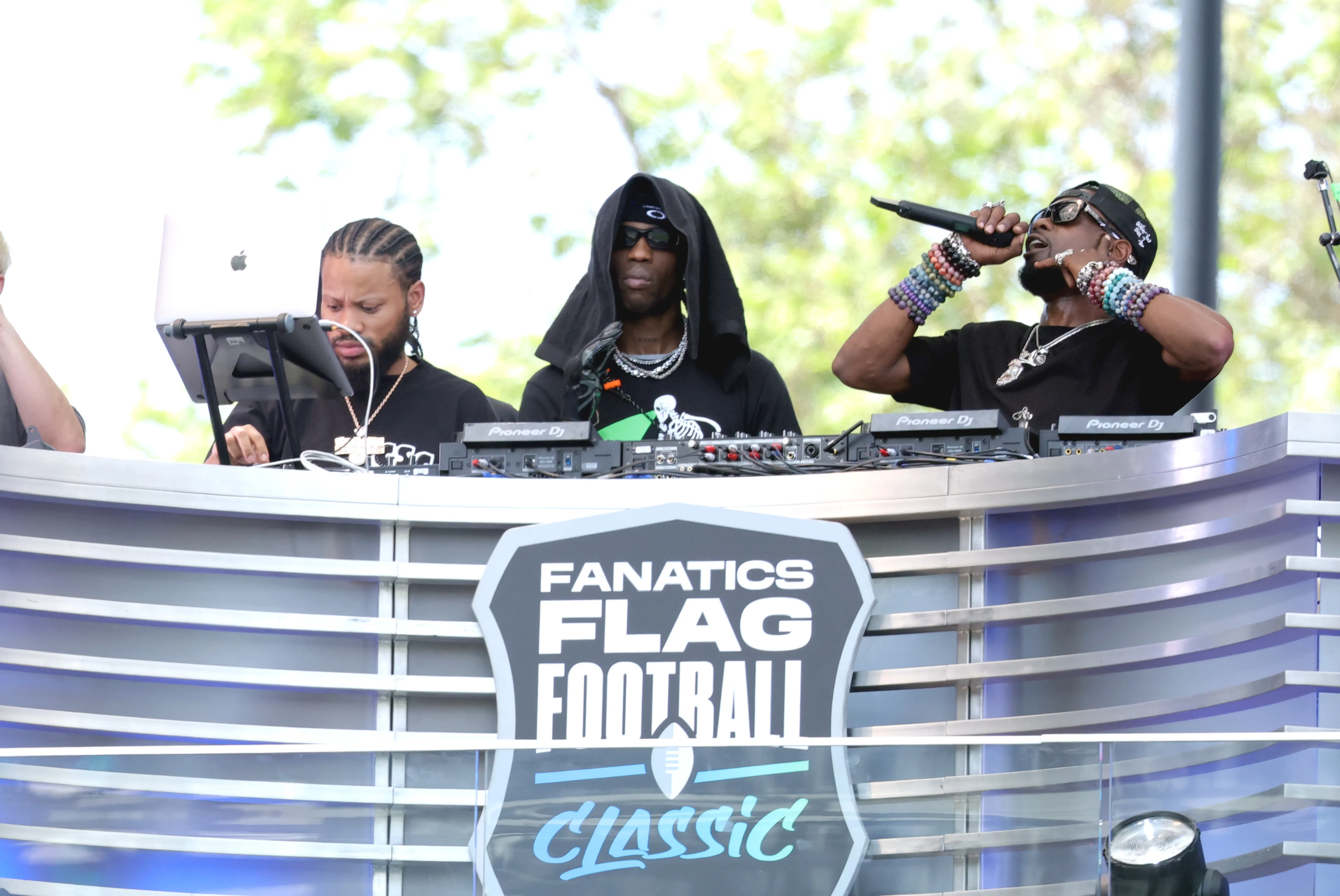 Three men perform at the Fanatics Flag Football Classic event, with one speaking into a microphone.