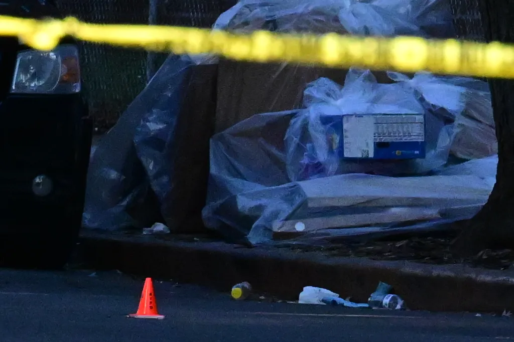 Crime scene with yellow tape, an orange traffic cone, and discarded items on the ground.