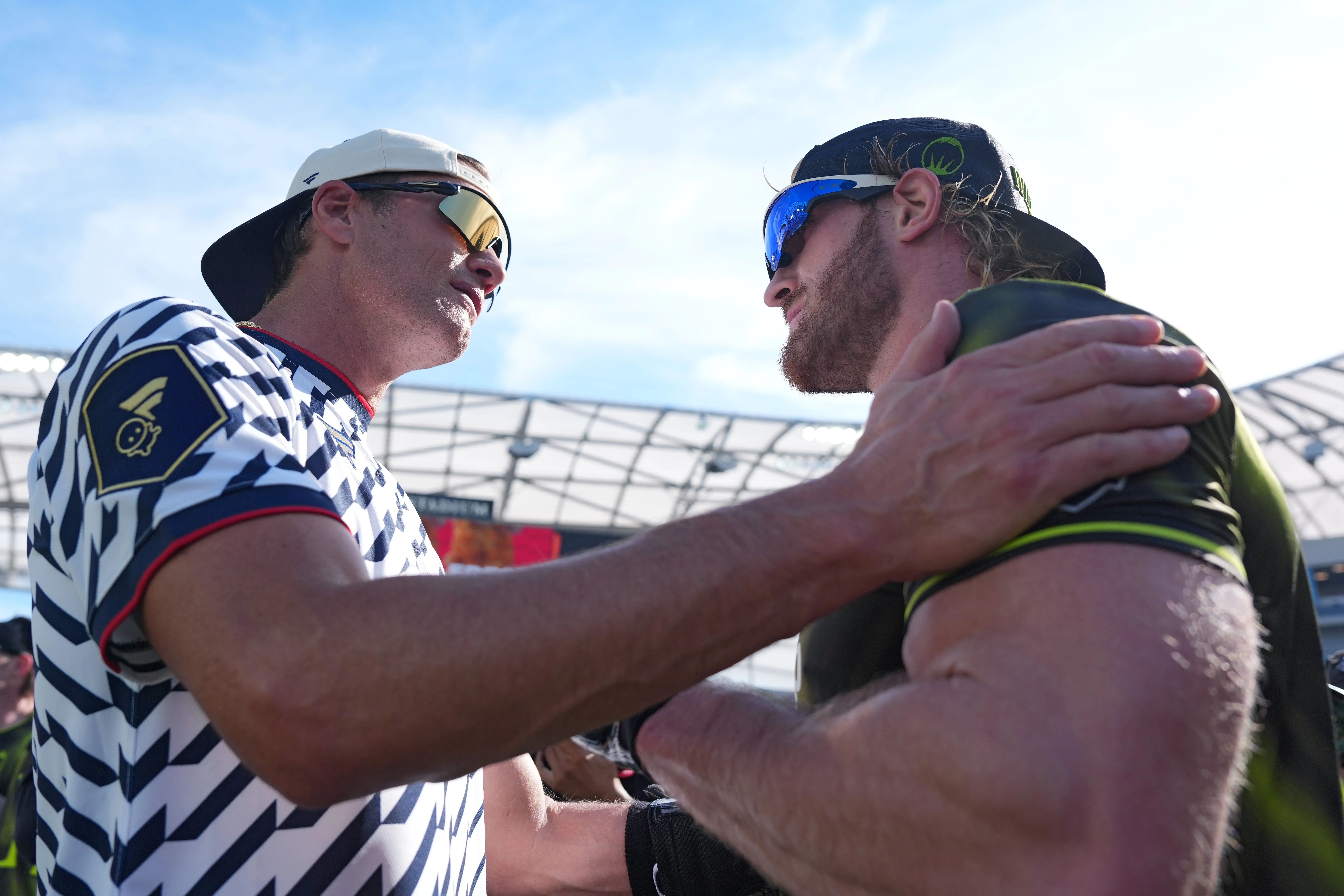 Two men in sports attire and sunglasses face each other on a field.