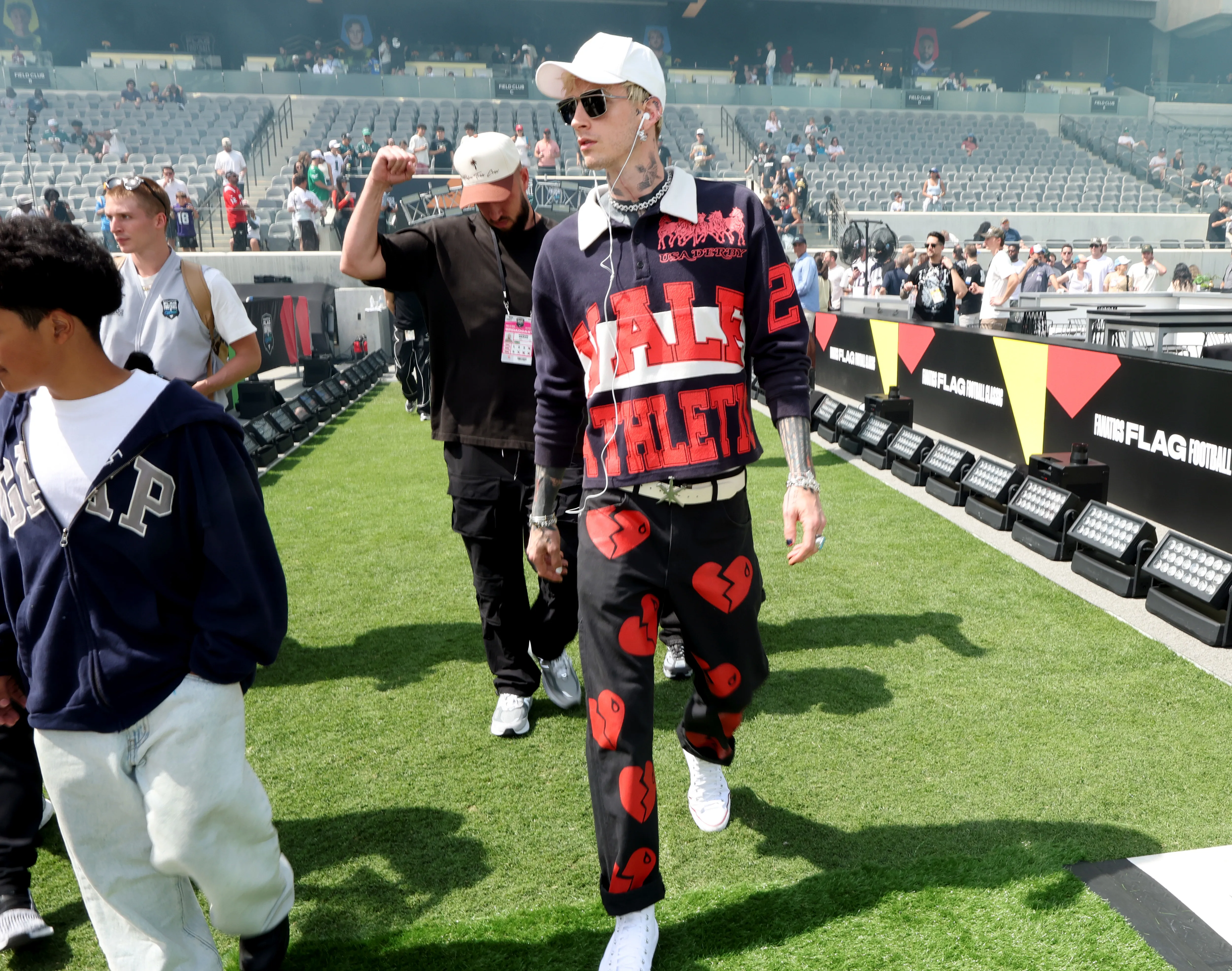 Machine Gun Kelly walking across a football field at the Fanatics Flag Football Classic.