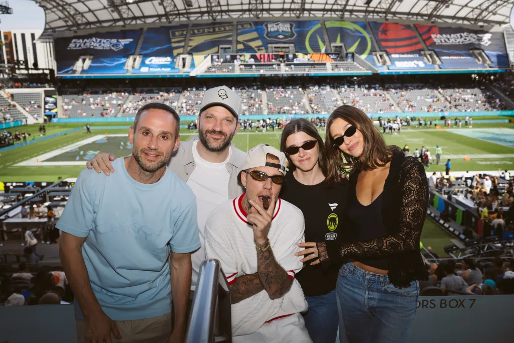 Five people, including Justin and Hailey Bieber, pose for a photo at a stadium.