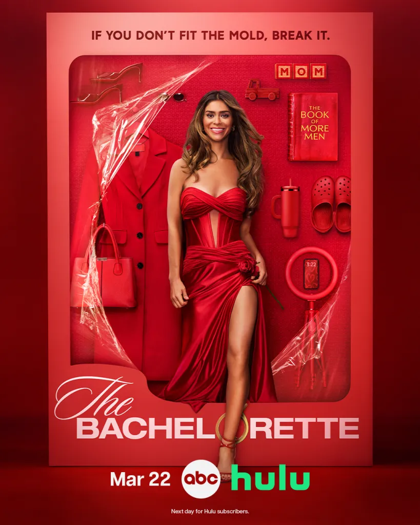 Taylor Frankie Paul in a red dress with a slit, holding a rose, inside a toy box-like setting with various items.