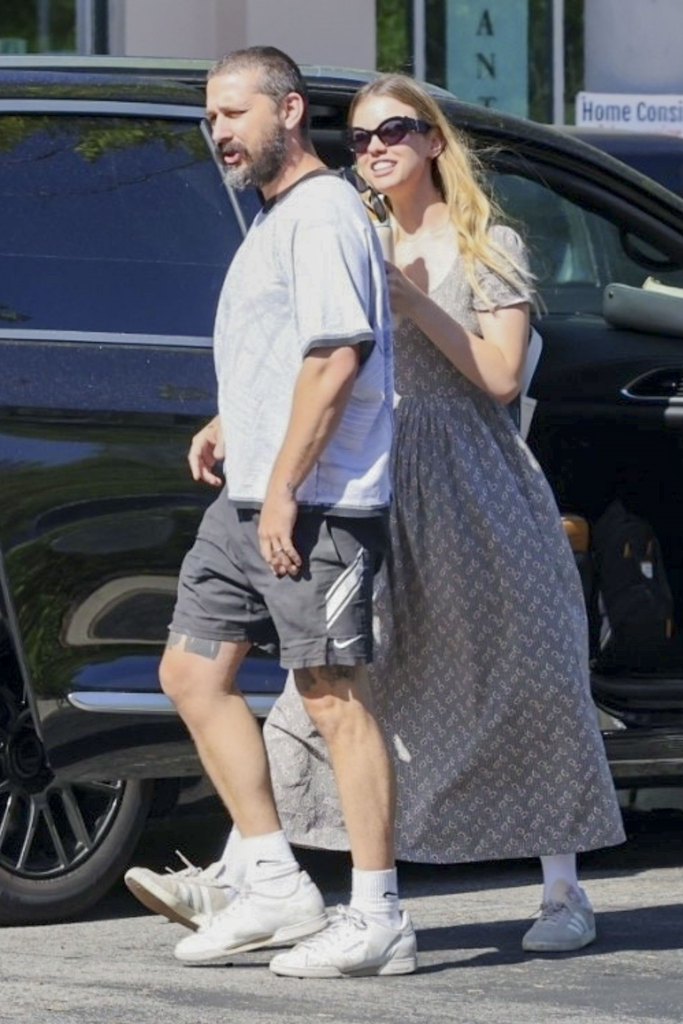 Shia LaBeouf and Mia Goth walking side-by-side with a car in the background.