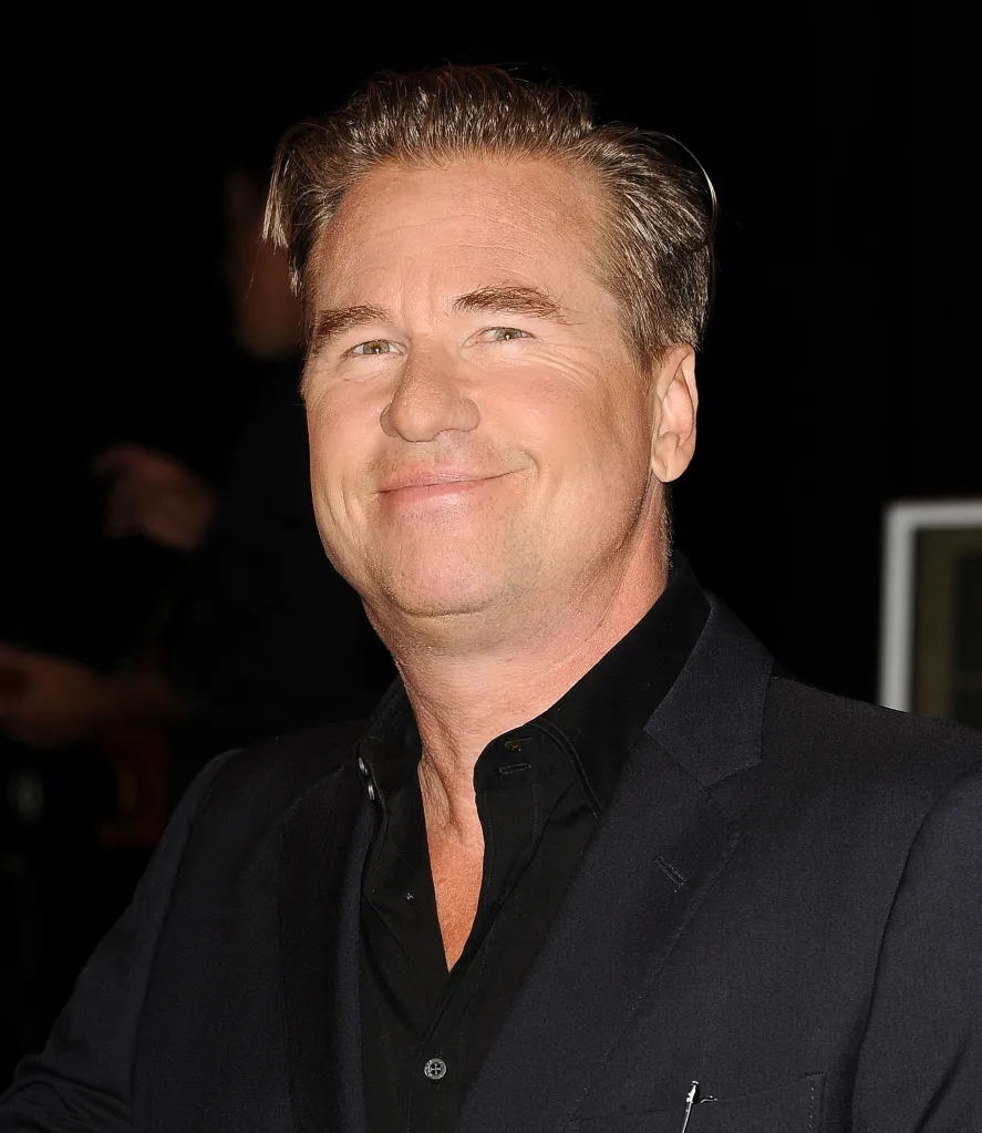 Actor Val Kilmer smiles, wearing a black shirt and suit jacket.