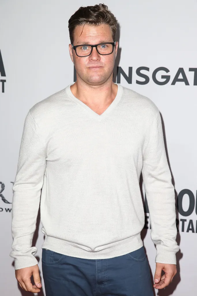 Actor Zachery Ty Bryan in a light v-neck sweater and blue pants.