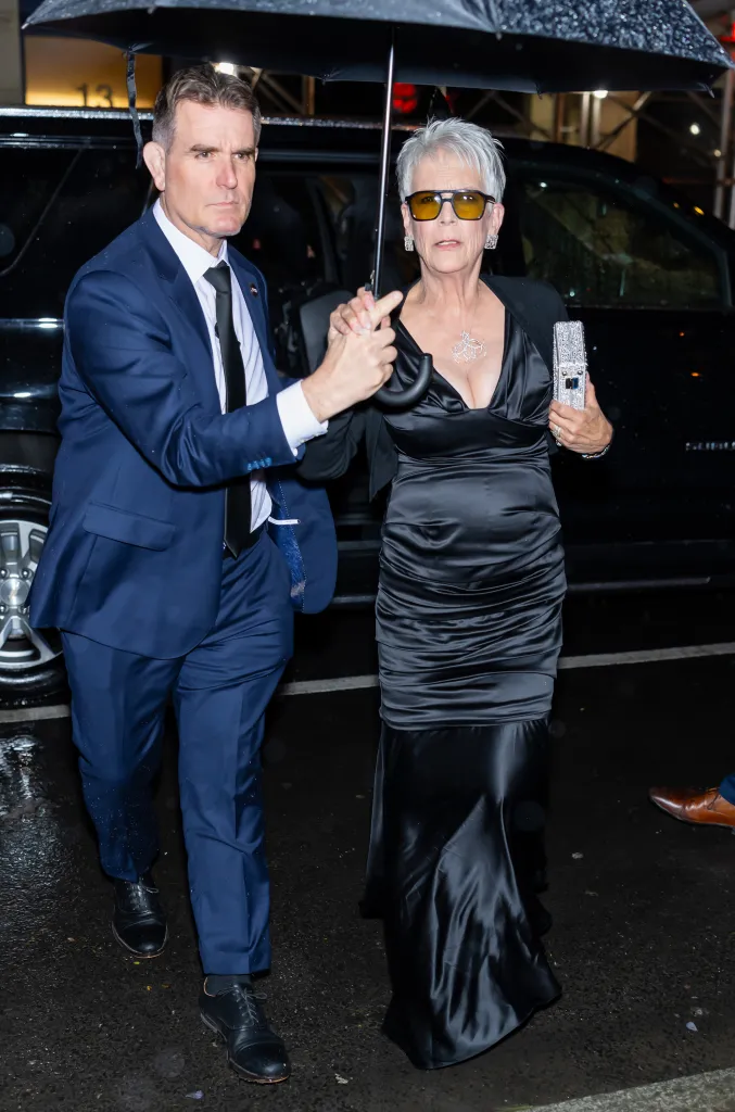 Actress Jamie Lee Curtis holding an umbrella with a man in a suit.