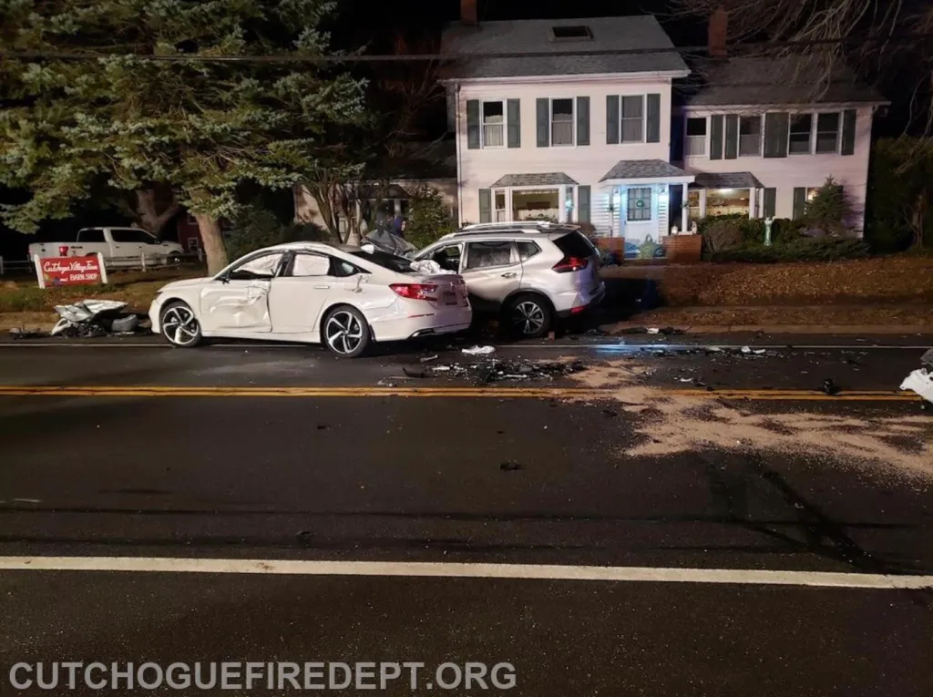 Two crashed cars, a white sedan and a silver SUV, on a road at night.