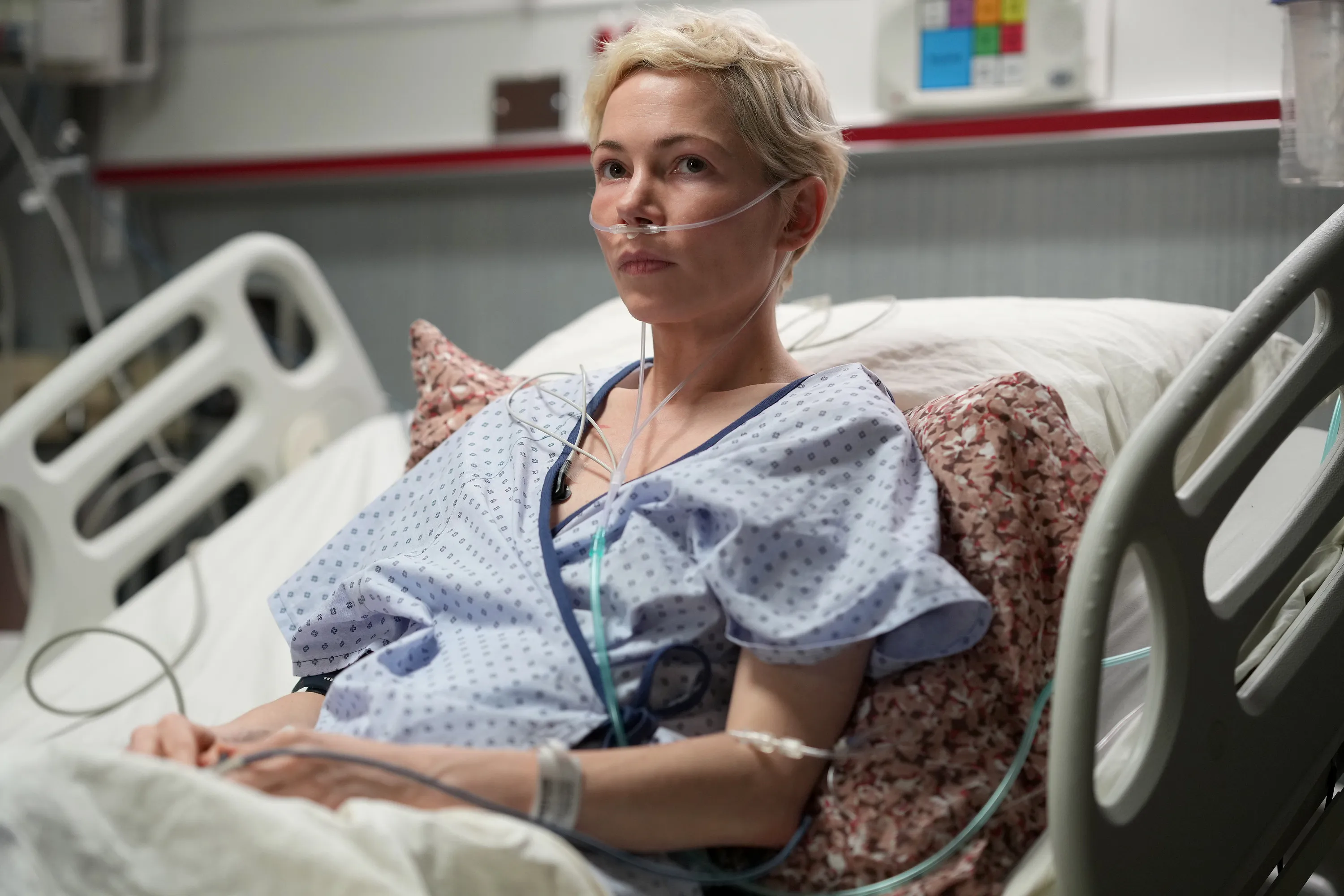Michelle Williams as Molly, wearing a hospital gown and a nasal cannula, sits up in a hospital bed.