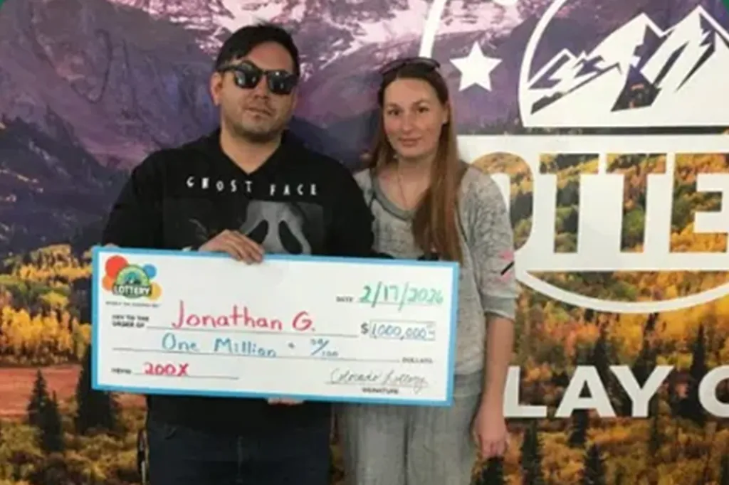 Jonathan G. and a woman holding an oversized check for one million dollars from the Colorado Lottery.