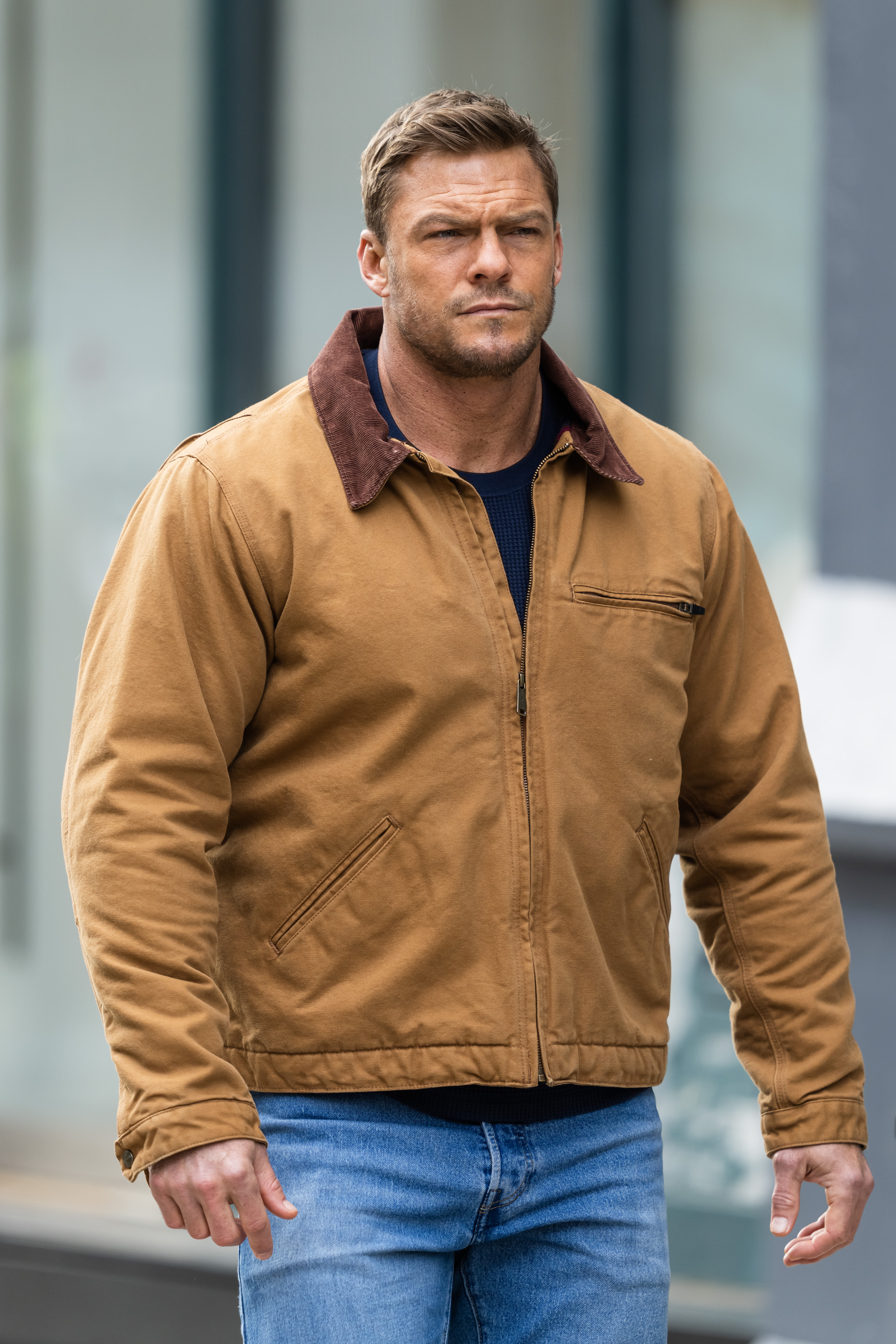 Alan Ritchson, dressed in a brown jacket and jeans, on the set of 