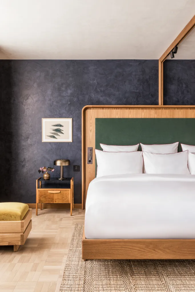 A bed with a wooden frame and green headboard next to a dark blue wall.